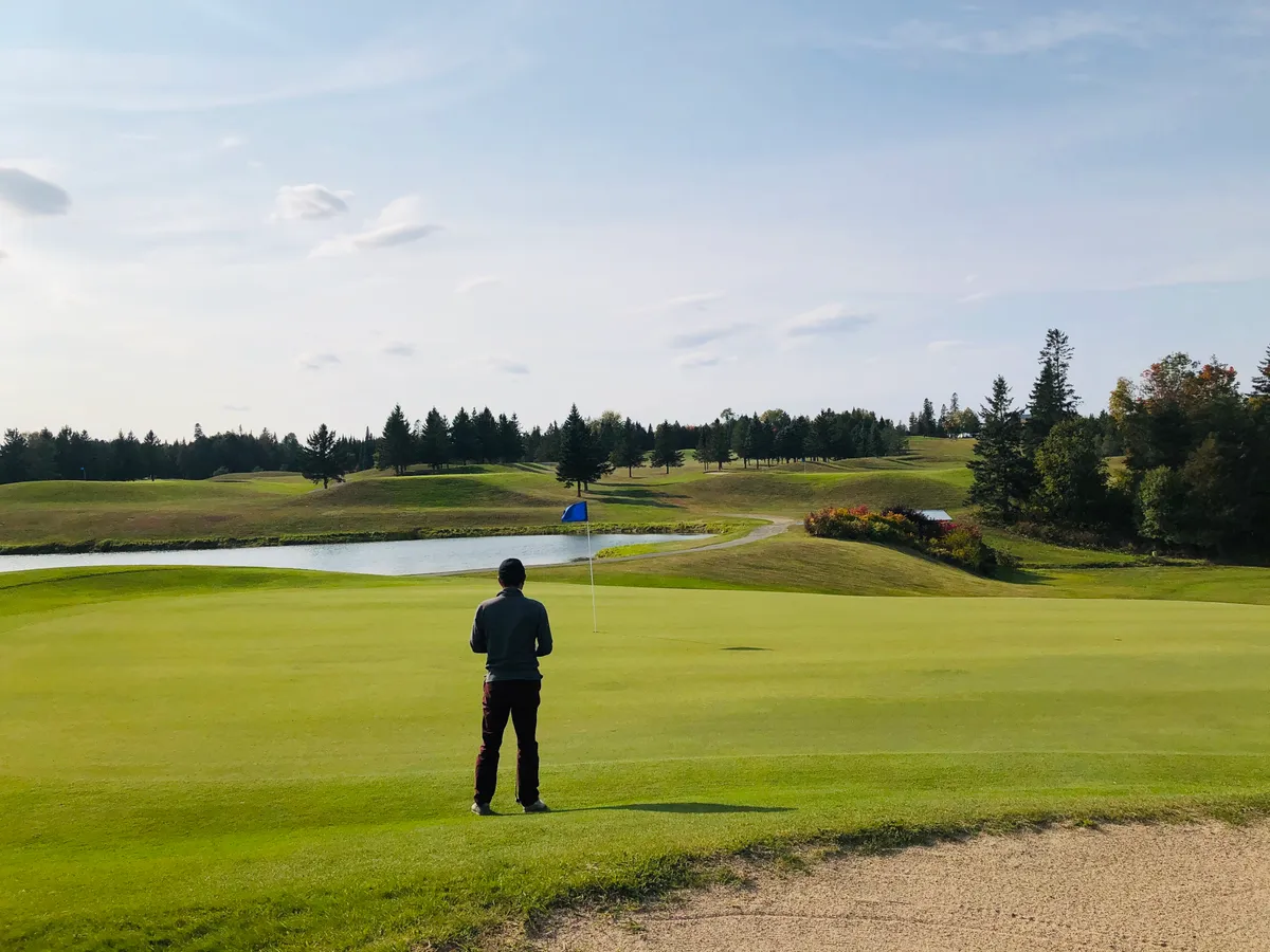 A golfer looking across a green beside water and trees at Covered Bridge