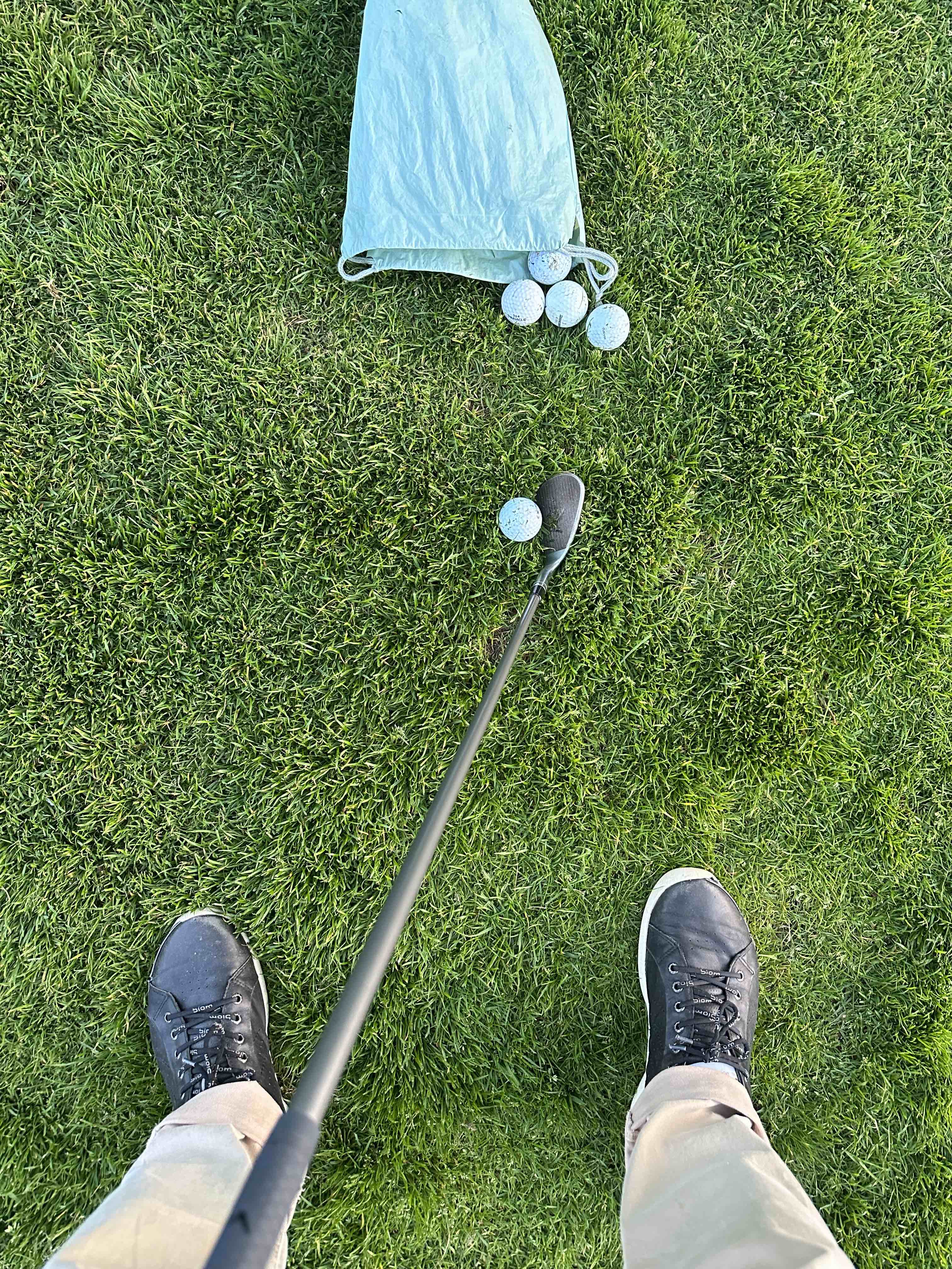 Golf balls, a cloth bag and a wedge on grass, seen from the player’s stance