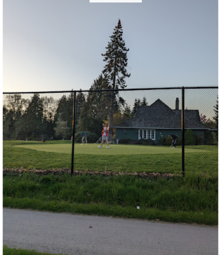 Golfers on a practice green behind a fence beside a clubhouse